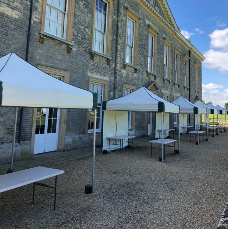 Ten 3m x 3m mini marquee gazebos set up in a prestigious row along the front of Althorp House stately home, fitted with trestle tables for a grand outdoor heritage event