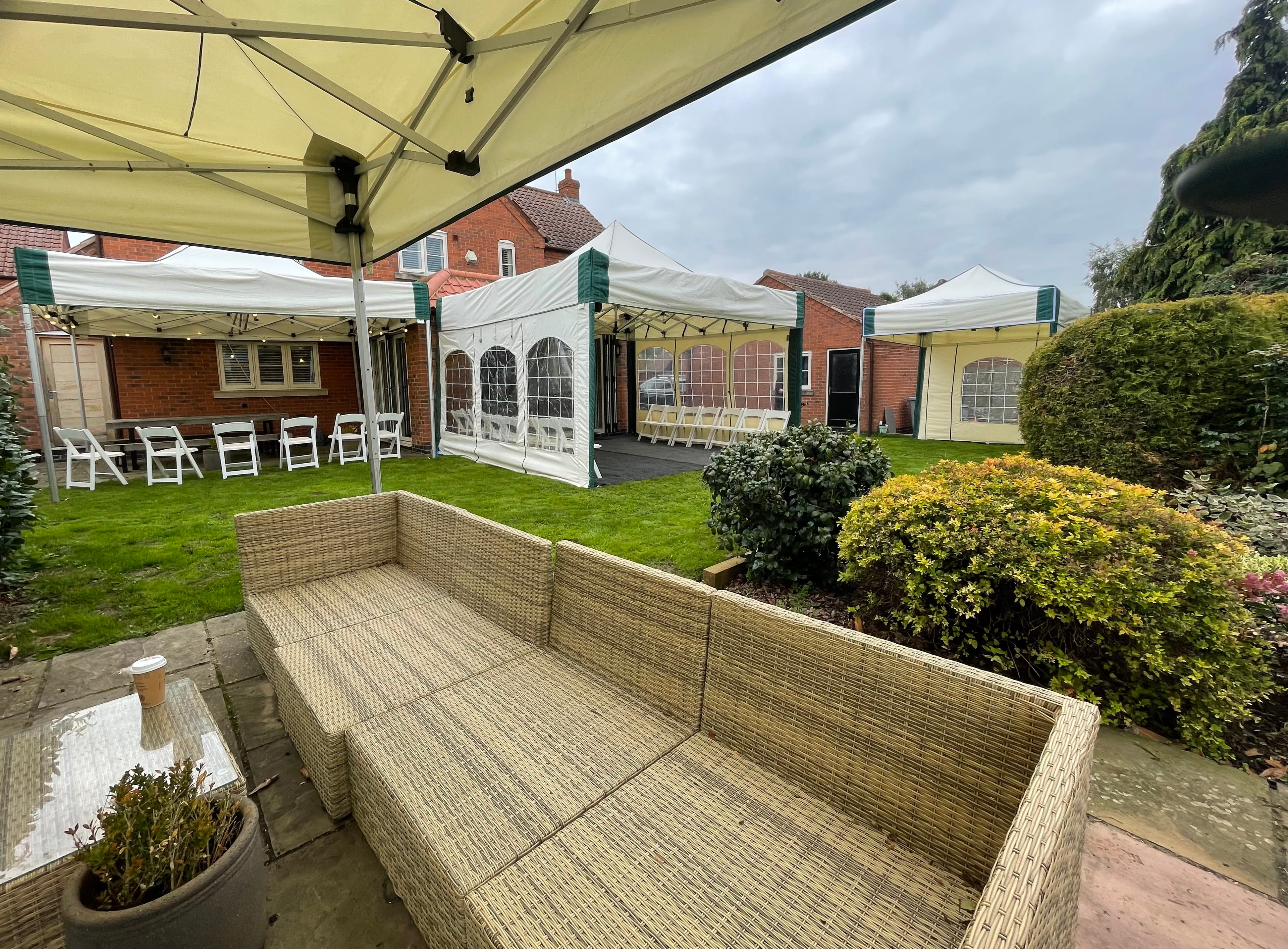 Multiple linked mini marquee gazebos (2 off 4.5m x 4.5m, 3m x 4.5m and 3m x 3m) set up in a private garden for a surprise 50th birthday party, with wicker lounge furniture and dressed tables