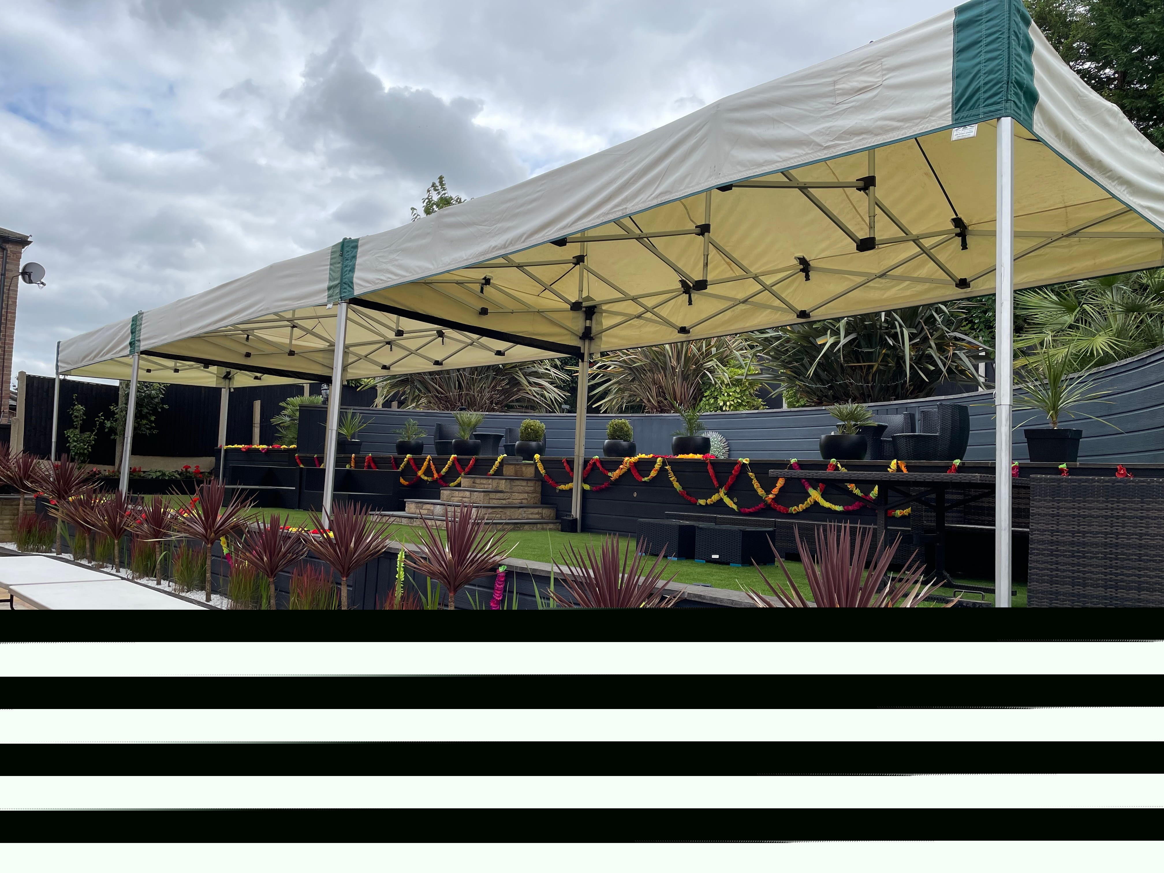 Two linked 6m x 3m mini marquee gazebos beautifully dressed with colourful floral garlands and long banquet tables for a garden celebration in Ravenshead