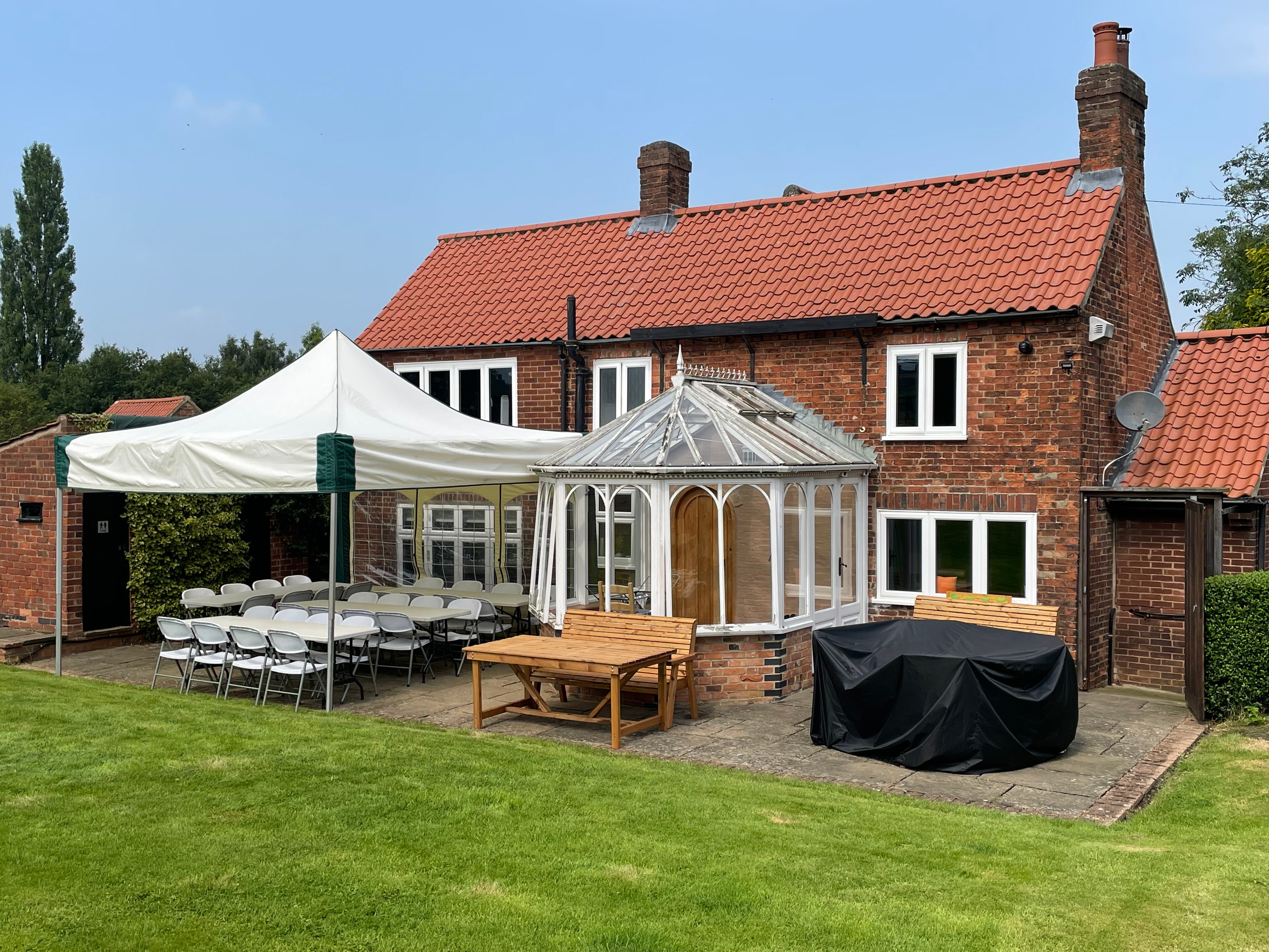 A 4.5m x 4.5m mini marquee gazebo set up alongside a countryside farmhouse for an intimate baby shower, with folding tables and chairs providing covered outdoor dining