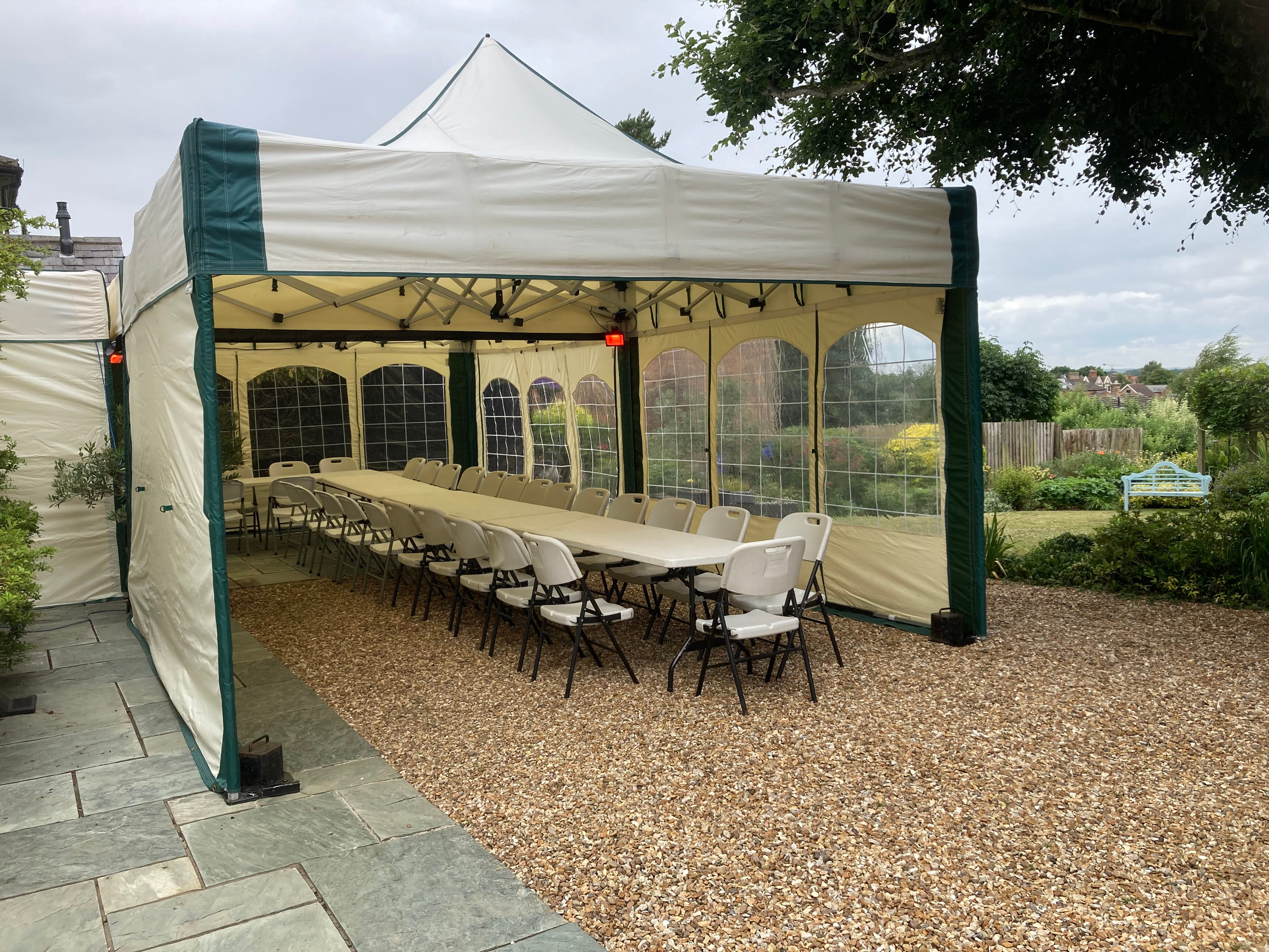 A 9m × 4.5m mini marquee created by linking two 4.5m structures in an L-shape configuration, featuring a long banquet table with chairs, clear window sidewalls and view over a country garden
