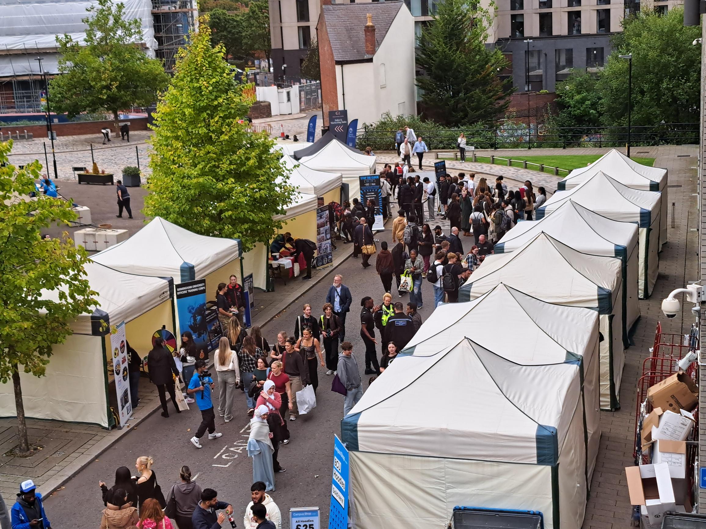 Multiple Premium Range 3m x 3m mini marquee gazebos deployed at Birmingham City University Union for a freshers fair, with rows of branded stalls and hundreds of students attending